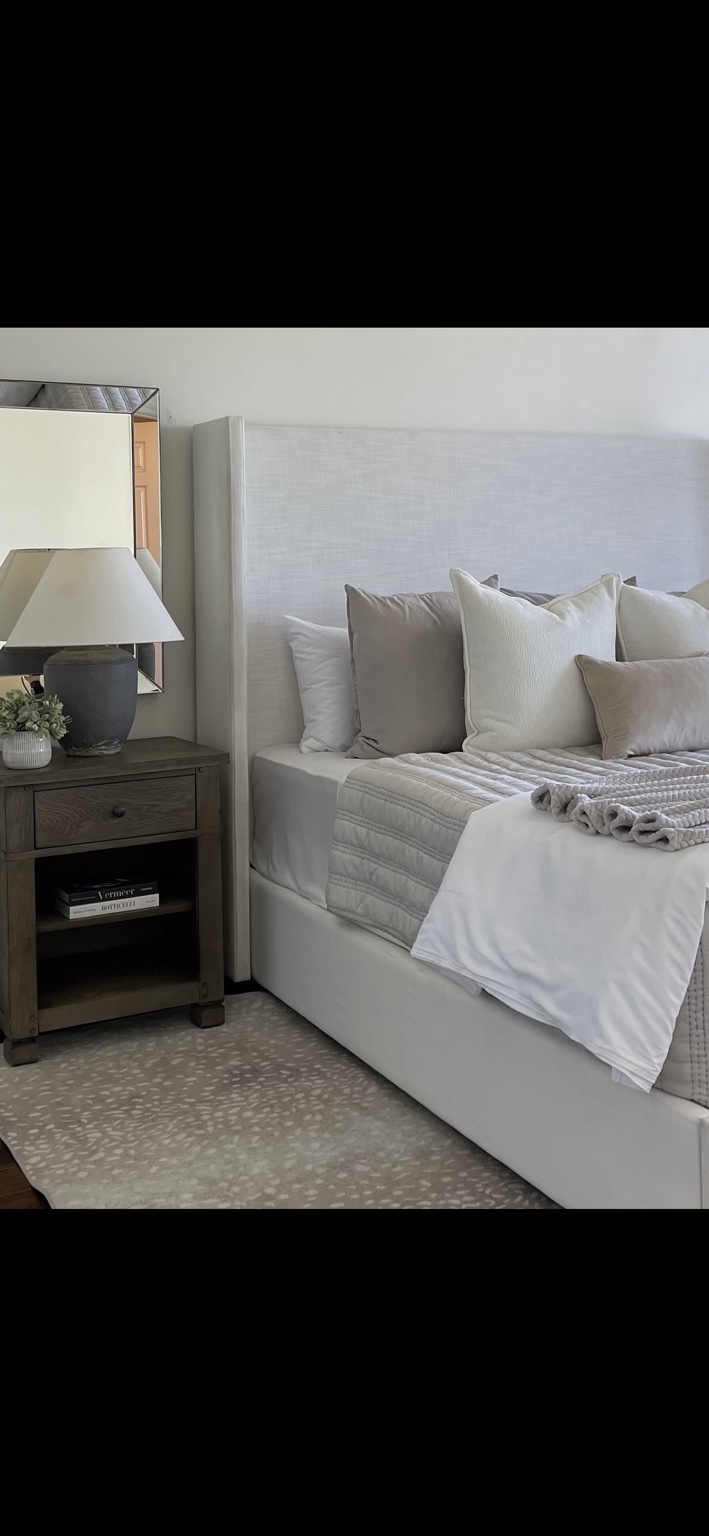 Bedroom with tailored neutral bedding, a wood nightstand, and a statement mirror