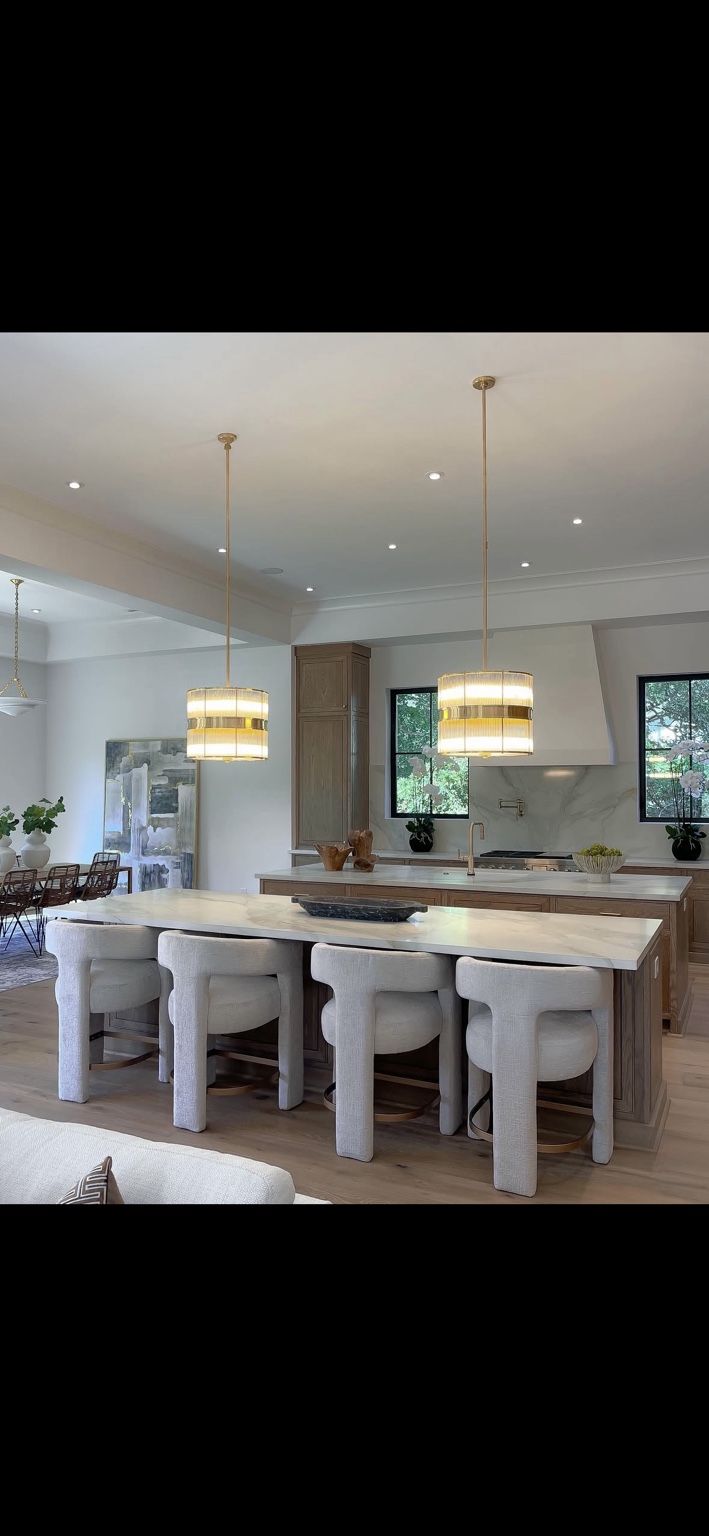 Kitchen with marble counters, gold pendant lights, and upholstered counter stools