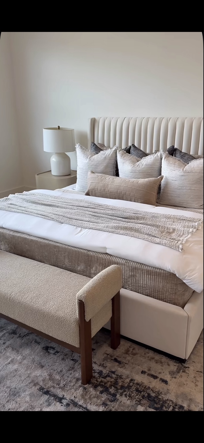Bedroom with a channel upholstered headboard, layered neutral pillows, and a textured bench